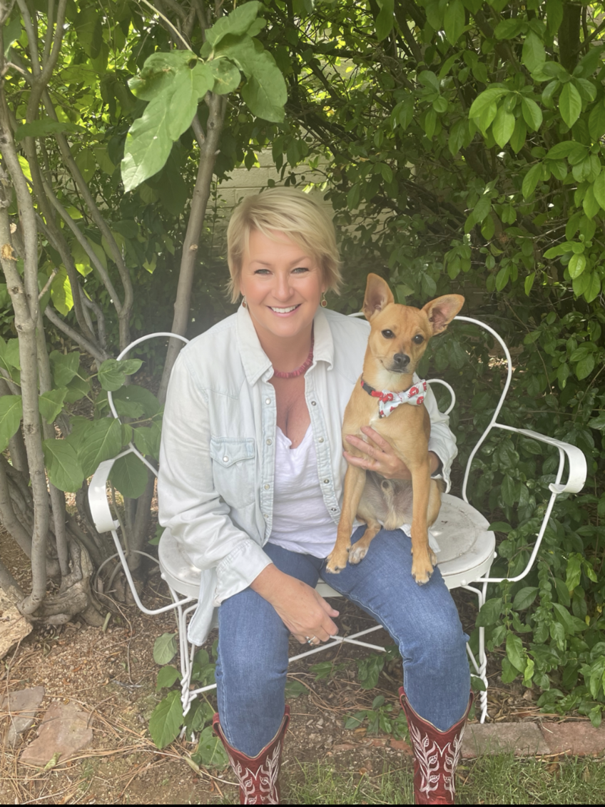 Susan Hawk seated in a white chair holding a small tan dog